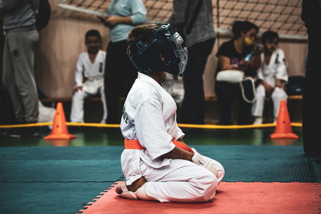 pexels photo 10355223 10355223 Boy in protective gear practices martial arts in indoor dojo setting surrounded by others.